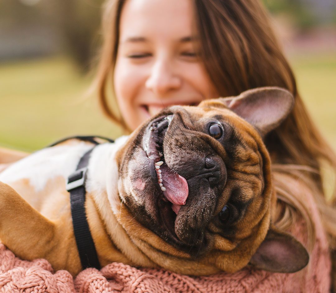 happy female holding bulldog in arms outside